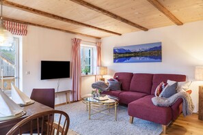 A living room with a red sofa, a flat-screen TV, a painting of mountains, and a wooden ceiling. - Apartment 'Lisbeth' with Shared Garden, Balcony, and Wi-Fi (Rottenbuch)