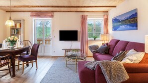A cozy living room with a wooden ceiling, a flat-screen TV, a red sofa, a dining table with chairs, and a bookshelf. - Apartment 'Lisbeth' with Shared Garden, Balcony, and Wi-Fi (Rottenbuch)