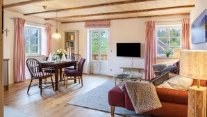 A cozy living room with wooden beams, a dining area with a table and chairs, a sofa, and a TV mounted on the wall. - Apartment 'Lisbeth' with Shared Garden, Balcony, and Wi-Fi (Rottenbuch)