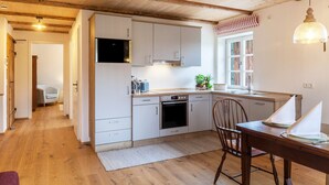 A modern kitchen with white cabinets, a built-in oven, and a dining area with a wooden table and chairs. - Apartment 'Lisbeth' with Shared Garden, Balcony, and Wi-Fi (Rottenbuch)