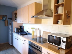 A modern kitchen with wooden cabinets, a built-in microwave, a stove, and a coffee maker. - Holiday Apartment 'Boven' at Timmeler Meer with Balcony and Wi-Fi (Timmel)