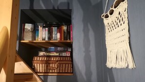 Ein Bücherregal mit Büchern, ein Wandbehang aus Makramee und ein Holztisch mit Tastatur.