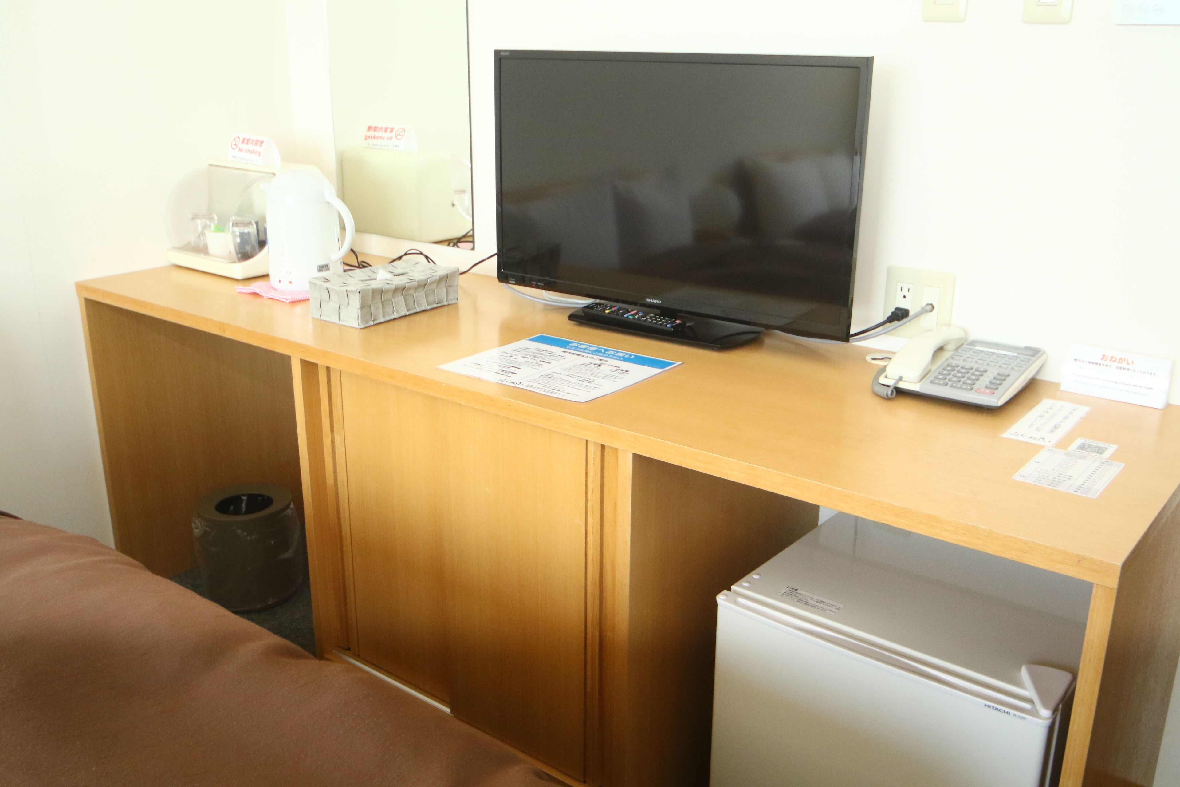 A hotel room with a wooden desk, a flat-screen TV, a small refrigerator, a coffee maker, and a telephone.