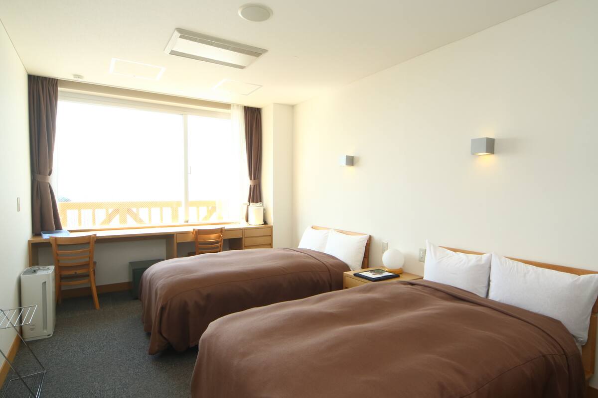 Ein Hotelzimmer mit zwei Betten, einem Schreibtisch und einem Fenster mit Vorhängen.