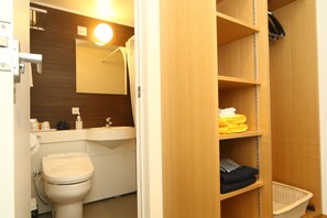 A bathroom with a toilet, sink, mirror, and wooden shelves with folded towels and a basket.