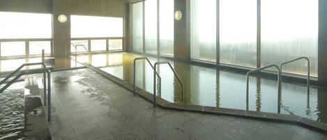 An indoor swimming pool with clear glass walls, metal handrails, and a tiled floor.