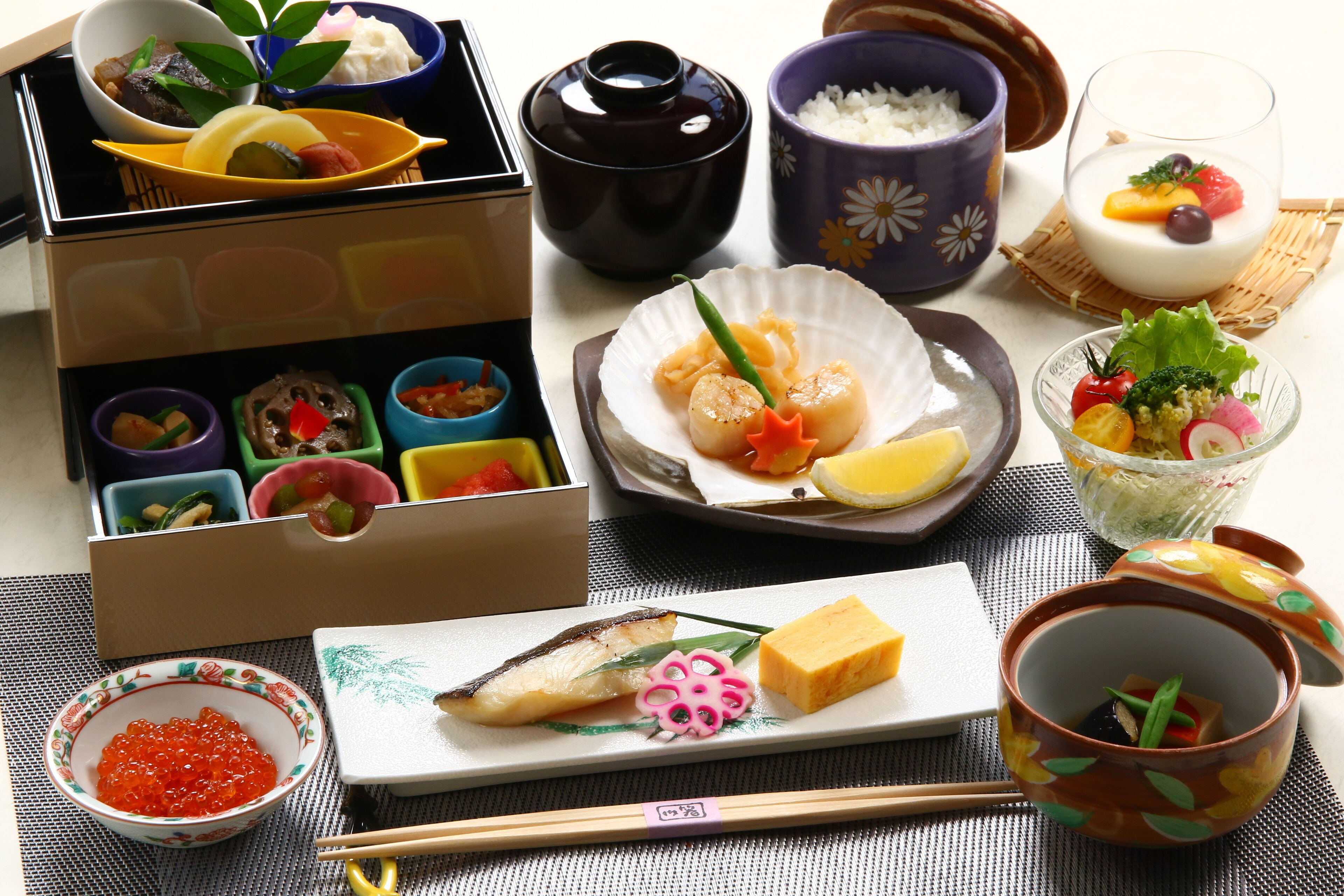 Une variété de plats japonais, notamment des sushis, des sashimis et des légumes marinés, présentés sur une table avec des baguettes et des bols.