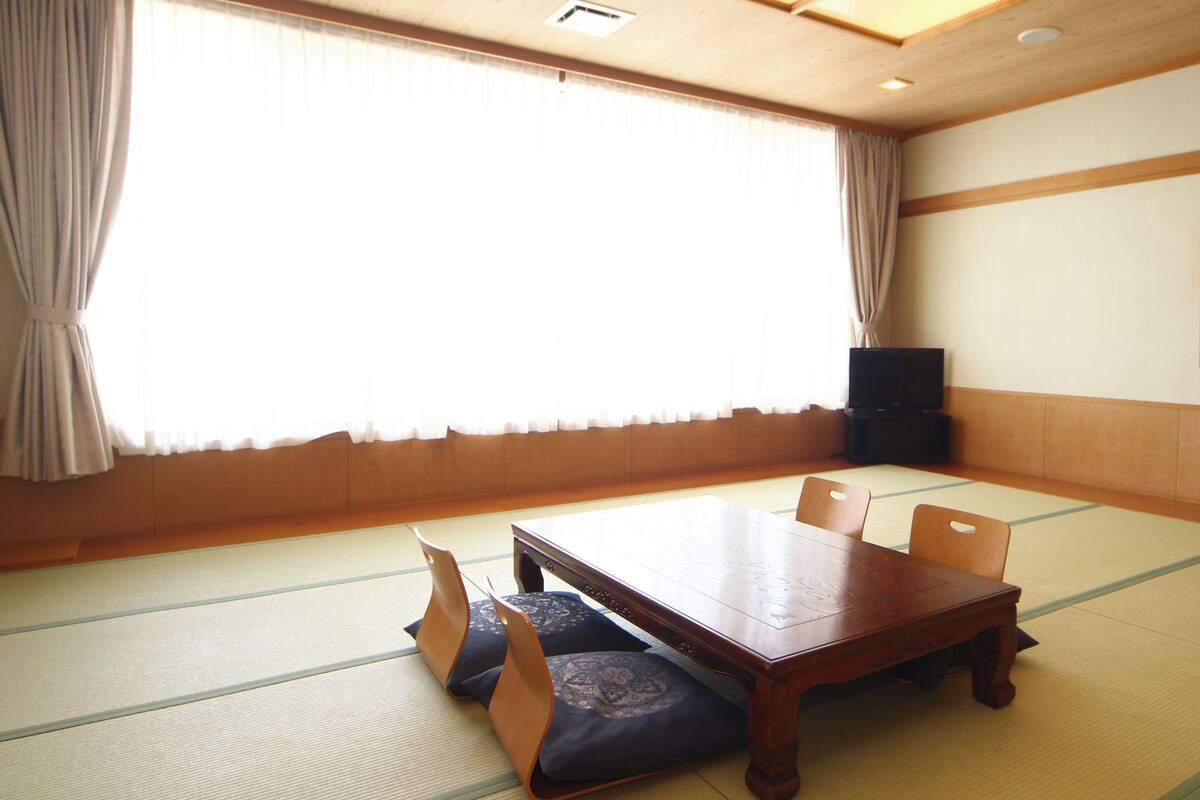 Ein traditioneller Tatami-Raum mit Holztisch, Stühlen und einem Fernseher.