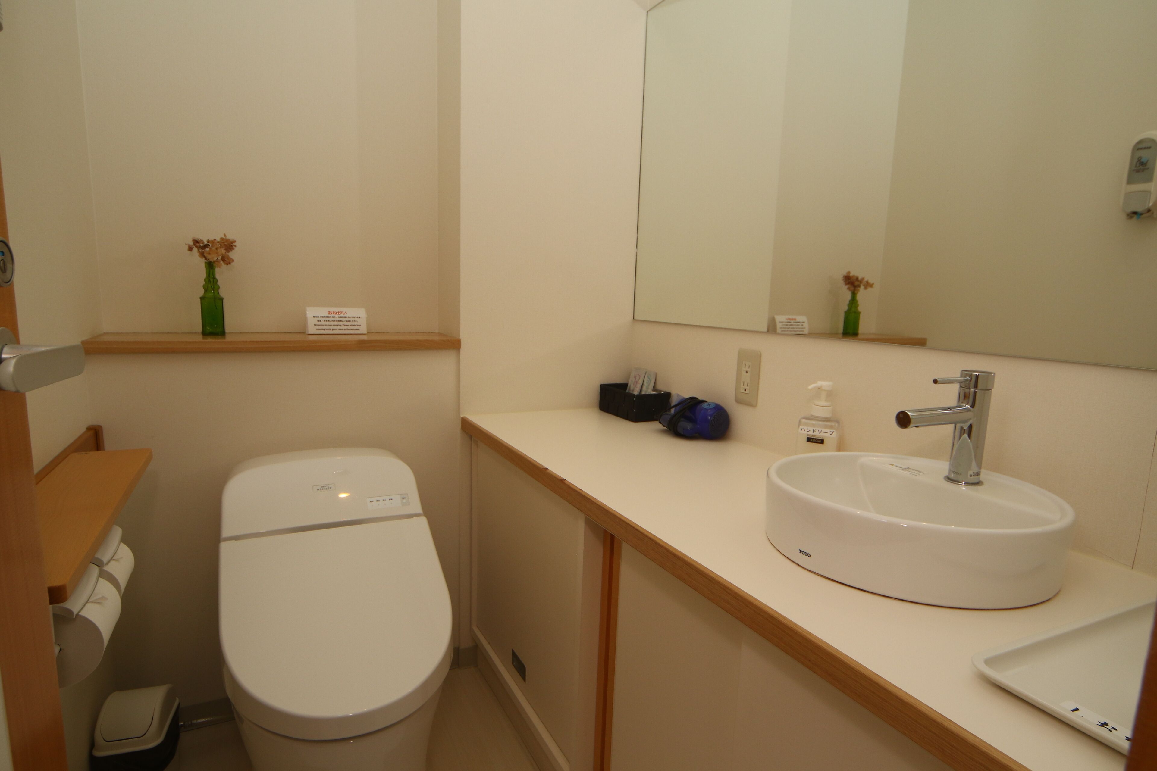 A small bathroom with a toilet, a sink, a mirror, and a shelf with toiletries.