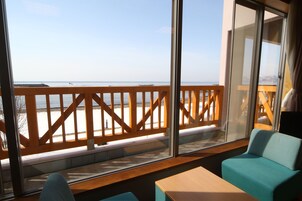 A balcony with a wooden railing, a view of the sea, and a seating area with a table and chairs.