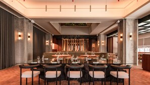A spacious dining area with a long table set for multiple guests, flanked by tall columns and modern lighting fixtures.
