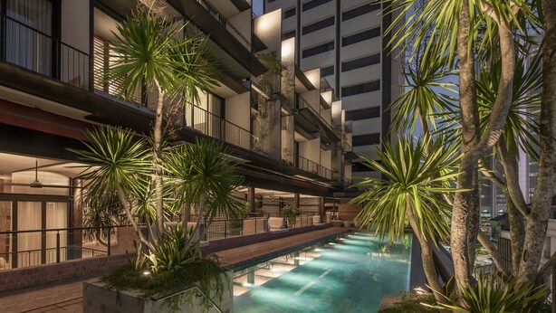 An indoor swimming pool with a modern design, surrounded by palm trees and a multi-level building with balconies.