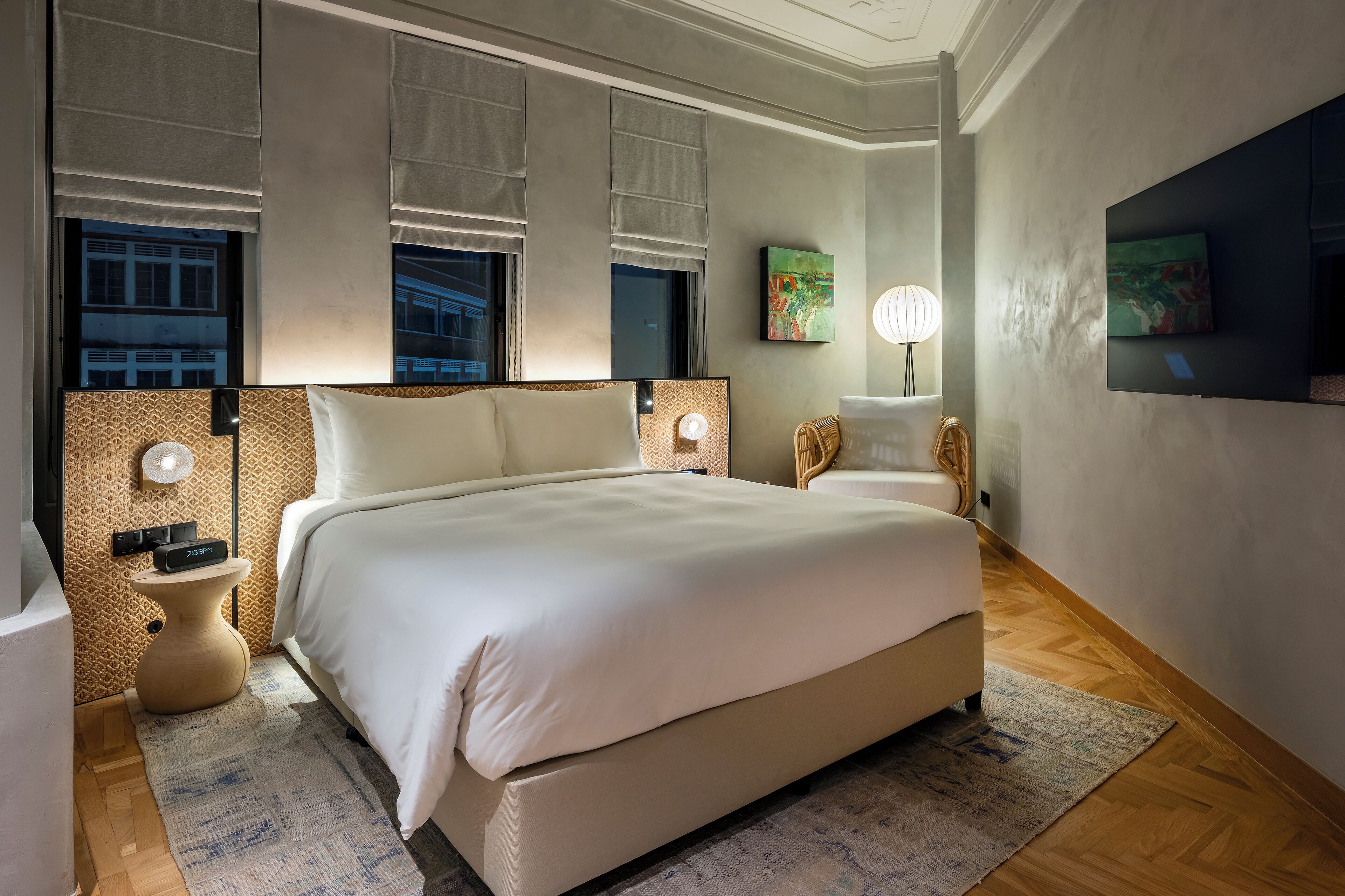 A modern hotel room with a large bed, bedside lamps, a flat-screen TV, and a decorative wall piece.