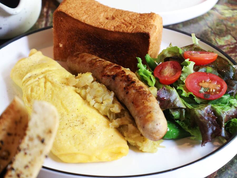 A plate with toast, sausage, scrambled eggs, and a salad.