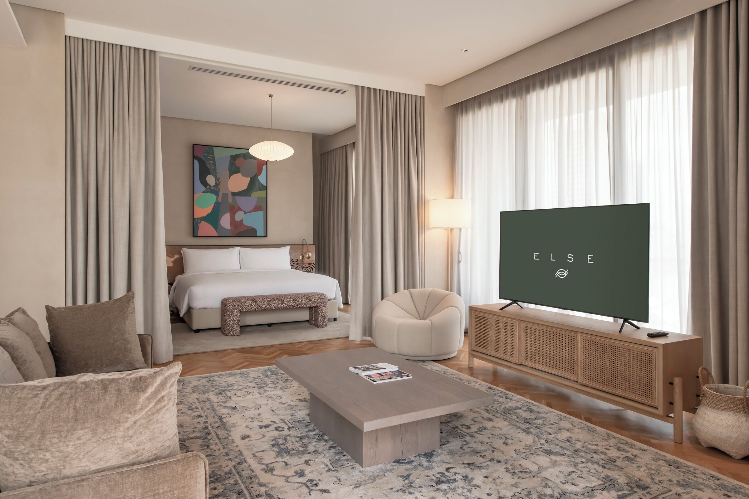 A hotel room with a bed, a sofa, a coffee table, a TV, and a large window with curtains.