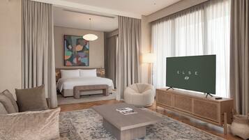 A hotel room with a bed, a sofa, a coffee table, a TV, and a large window with curtains.