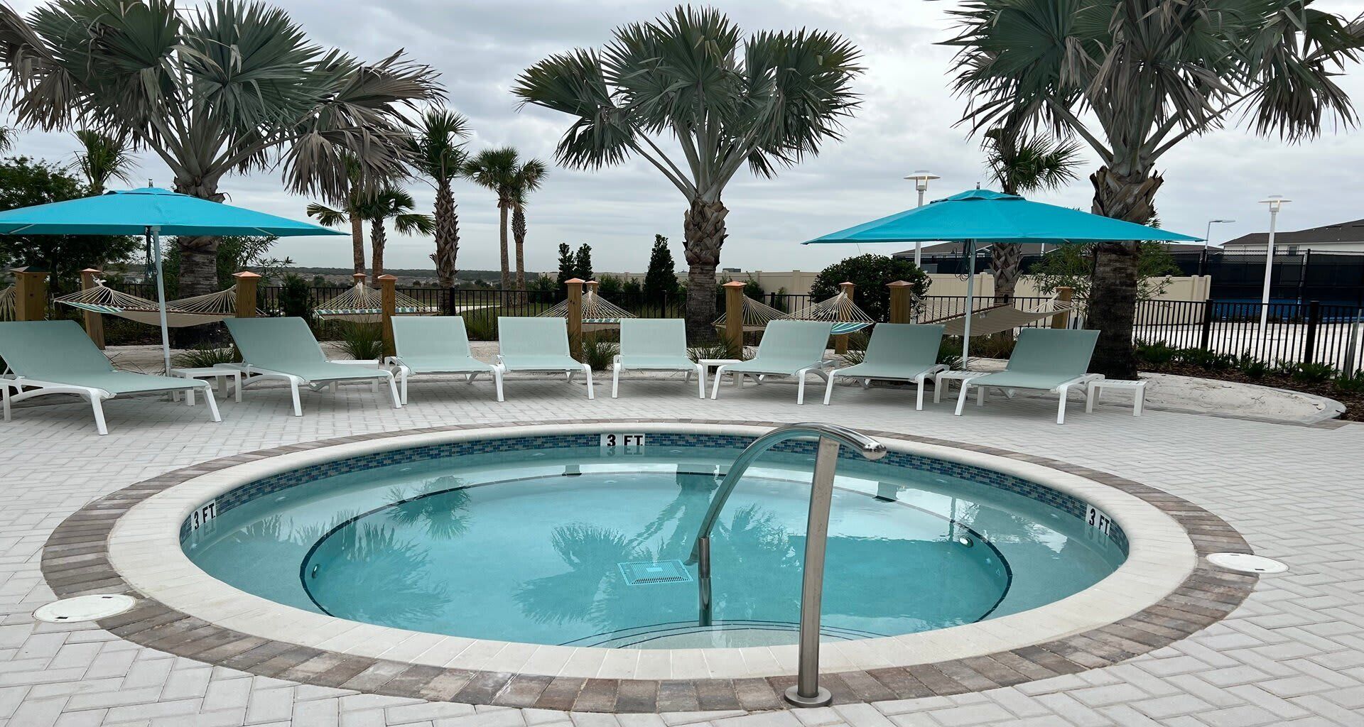Ein kreisförmiger Pool mit Liegestühlen und Sonnenschirmen, umgeben von Palmen.