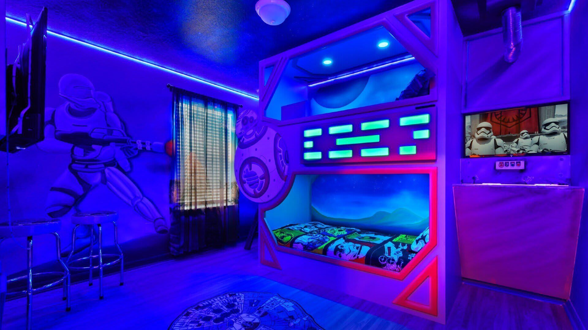 A room with bunk beds, a window with blinds, and a wall-mounted TV.