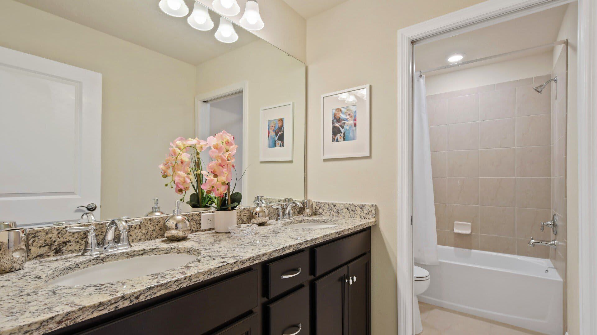 A bathroom with a granite countertop, a double sink, a large mirror, and a shower area.
