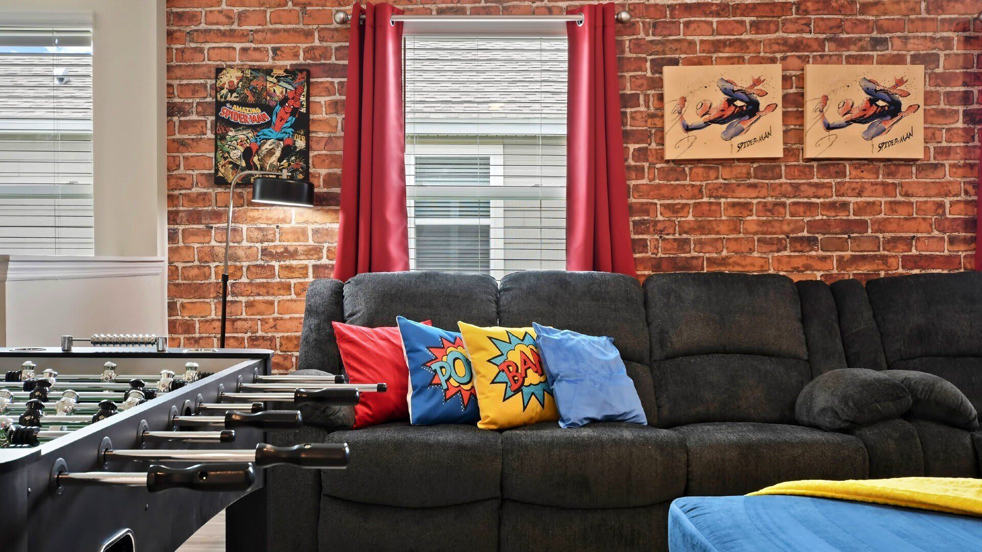 A cozy living room with a brick wall, a sofa, colorful pillows, and a foosball table.