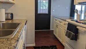 A kitchen with a granite countertop, stainless steel sink, white cabinets, and a black door. - Tucson Pool House, a vacation home with easy access to all Tucson offers (Tucson)