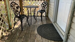 Une terrasse en bois avec deux tables et chaises en métal, une porte blanche et une clôture à treillis.