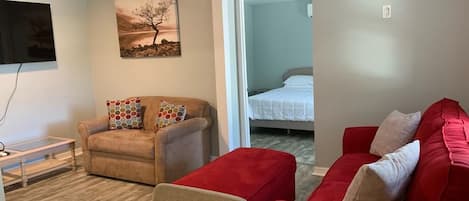 En kompakt opholdsstue med sofa, stol, lille bord og seng.