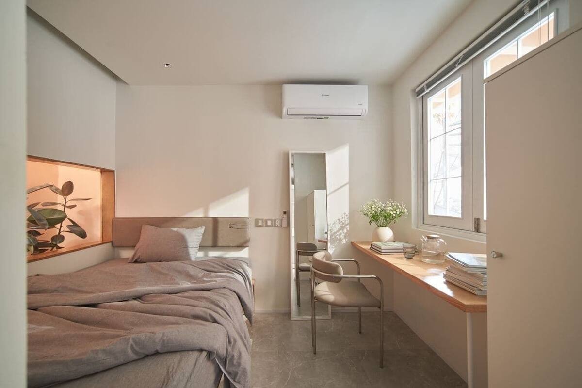 A bedroom with a bed, a desk, a chair, a mirror, and a window.