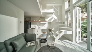 Um espaço moderno de estar com escada, área de cozinha e sofá verde.