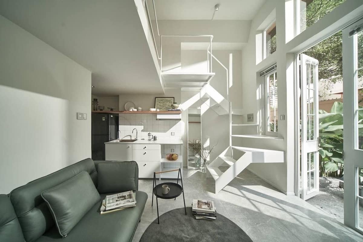 A modern living space with a staircase, a kitchen area, and a green sofa.
