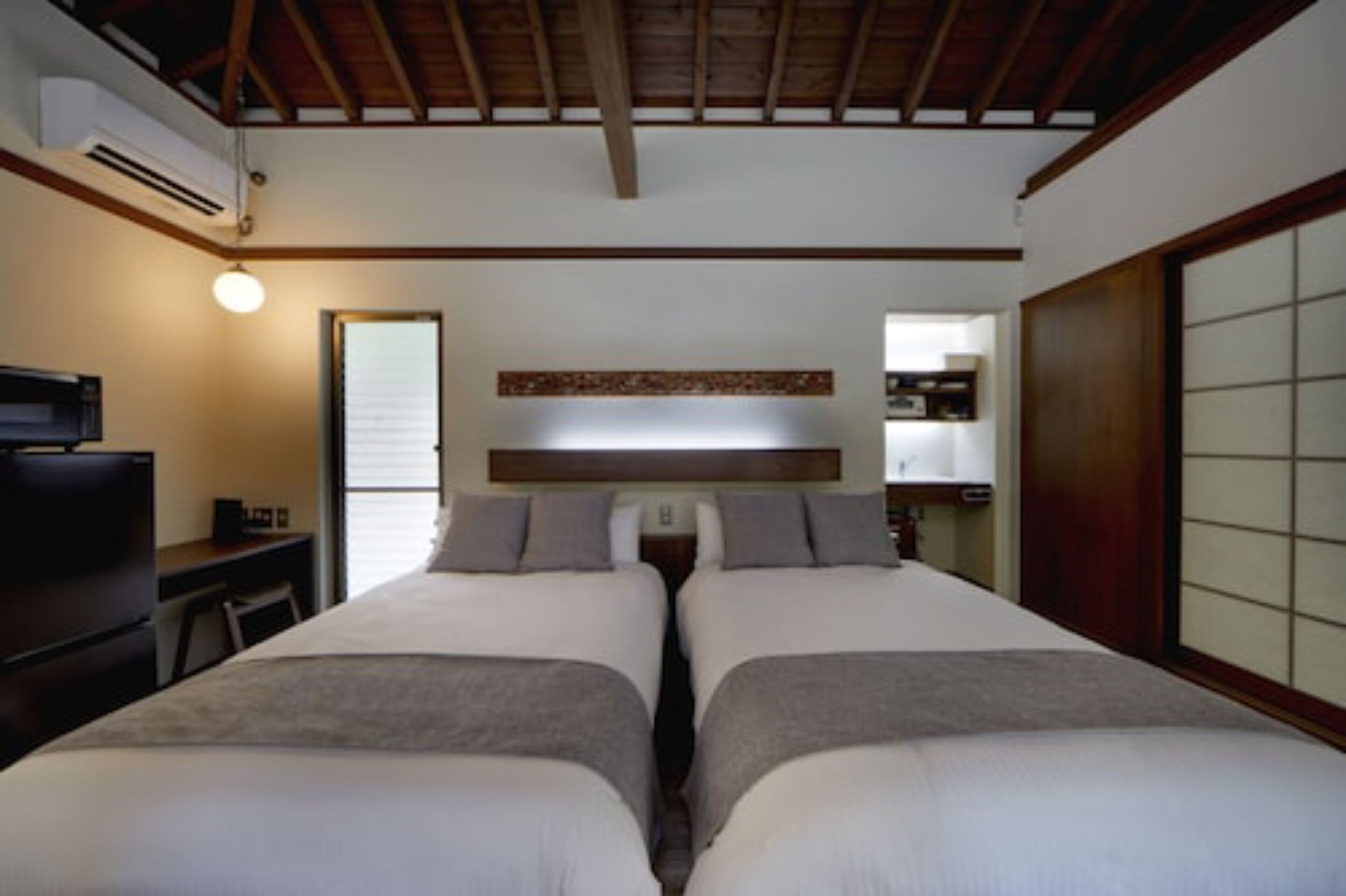 A hotel room with two beds, a desk, a TV, and a sliding door.