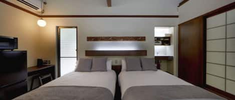 A hotel room with two beds, a desk, a TV, and a sliding door.