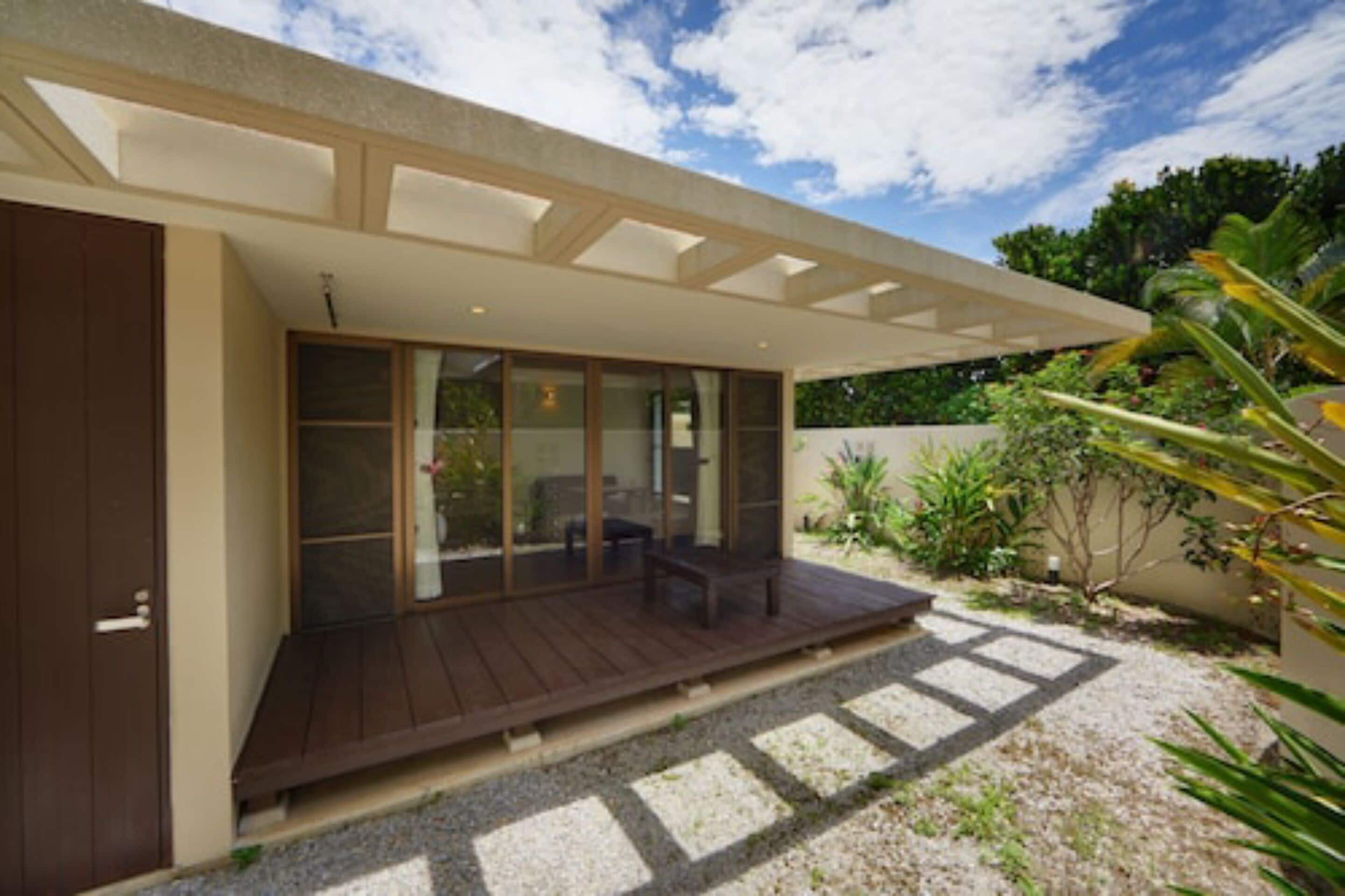 A modern house with a covered patio, large sliding glass doors, and a gravel driveway.