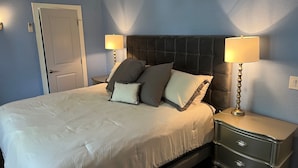 Un lit bien fait, recouvert d’une couette blanche et agrémenté de plusieurs oreillers, avec deux tables de chevet de chaque côté, sur lesquelles sont posées des lampes.