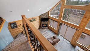 L’intérieur d’un chalet en bois est doté d’une cheminée en pierre, d’un canapé et de grandes fenêtres qui offrent une vue sur la forêt environnante.