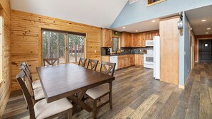 Une cuisine spacieuse avec des meubles en bois, un coin repas doté d’une grande table et de chaises, et une vue sur l’extérieur grâce à une porte-fenêtre coulissante.