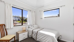 Una camera da letto con un letto singolo, una sedia di legno, un comodino e due finestre con tende.