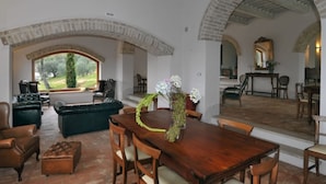 Uma sala de jantar com mesa de madeira, cadeiras e um vaso de flores. Apresenta paredes de tijolos em arco e vista para o exterior.