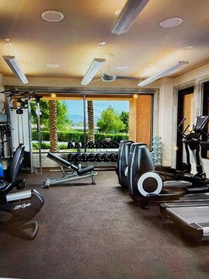 A gym with cardio equipment, weight benches, and dumbbells.