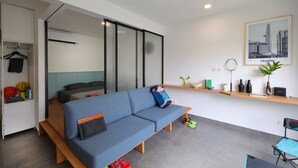 Een moderne woonkamer met een bank, een bed, een bijzettafeltje en een wandplank met decoratieve objecten.
