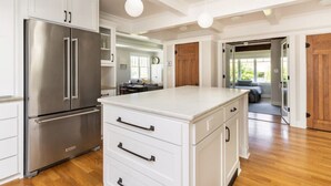 A modern kitchen with white cabinetry, a stainless steel refrigerator, and a large island with drawers. - Main house at 126 · Modern 2 Bedroom unit in a 1915 Craftsman home (Kirkland)