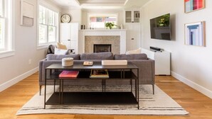 A living room with a fireplace, a sofa, a coffee table, and a TV. - Main house at 126 · Modern 2 Bedroom unit in a 1915 Craftsman home (Kirkland)