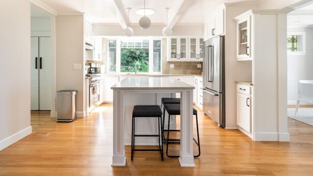 A spacious kitchen with a central island, white cabinetry, and a large window providing natural light. - Main house at 126 · Modern 2 Bedroom unit in a 1915 Craftsman home (Kirkland)