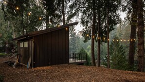 A cabin with a deck, surrounded by trees and string lights. - Panoramic Riverside and Lush Forests Views, Pet Friendly, New Décor, Steps Away From Dockside (West Linn)