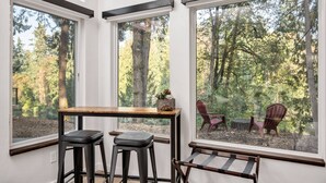 A room with three large windows, a wooden table, two black stools, and a bench. - Panoramic Riverside and Lush Forests Views, Pet Friendly, New Décor, Steps Away From Dockside (West Linn)