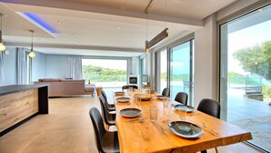 Una zona pranzo moderna con un tavolo di legno apparecchiato per sei persone, un divano e una TV sullo sfondo.