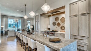 Una cocina moderna con una isla de mármol, luces colgantes y un ventanal grande.