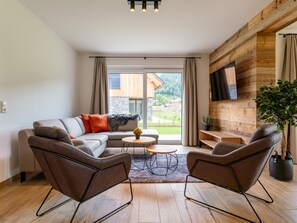 Een moderne woonkamer met een bank, twee fauteuils, een salontafel en een televisie bevestigd aan een houten wand.