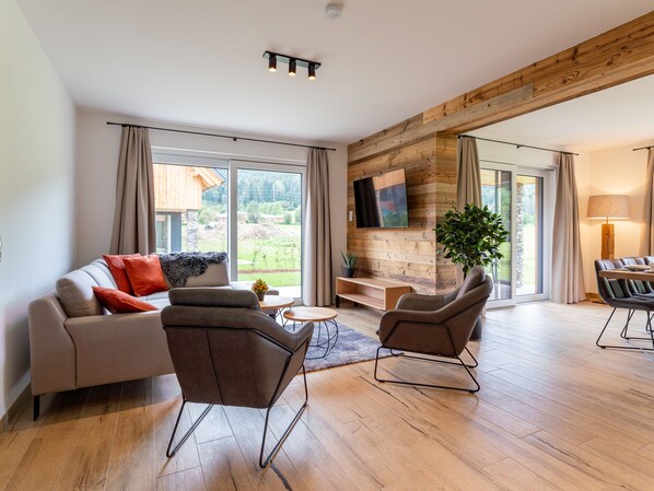 A modern living room with a wooden ceiling, a sofa, two armchairs, a coffee table, and a TV mounted on a wooden wall. - Luxurious house with sauna close to ski area (Kreischberg)