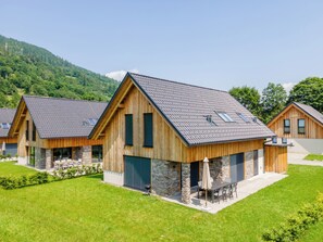 Une maison moderne en bois, dotée de fondations en pierre, de grandes fenêtres et d’une pelouse bien entretenue.